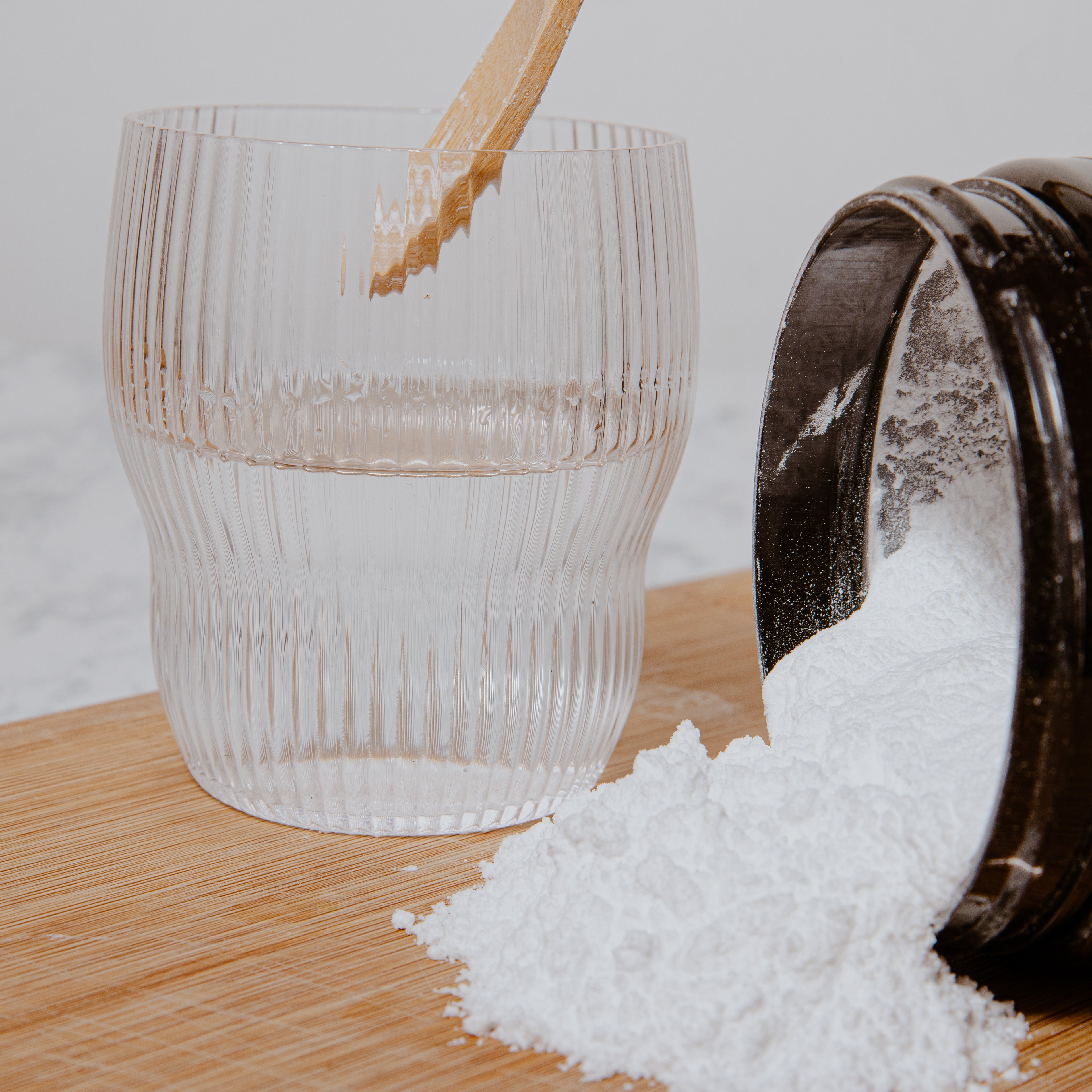 Wooden spoon scooping white powder from a container onto a glass on a wooden surface.