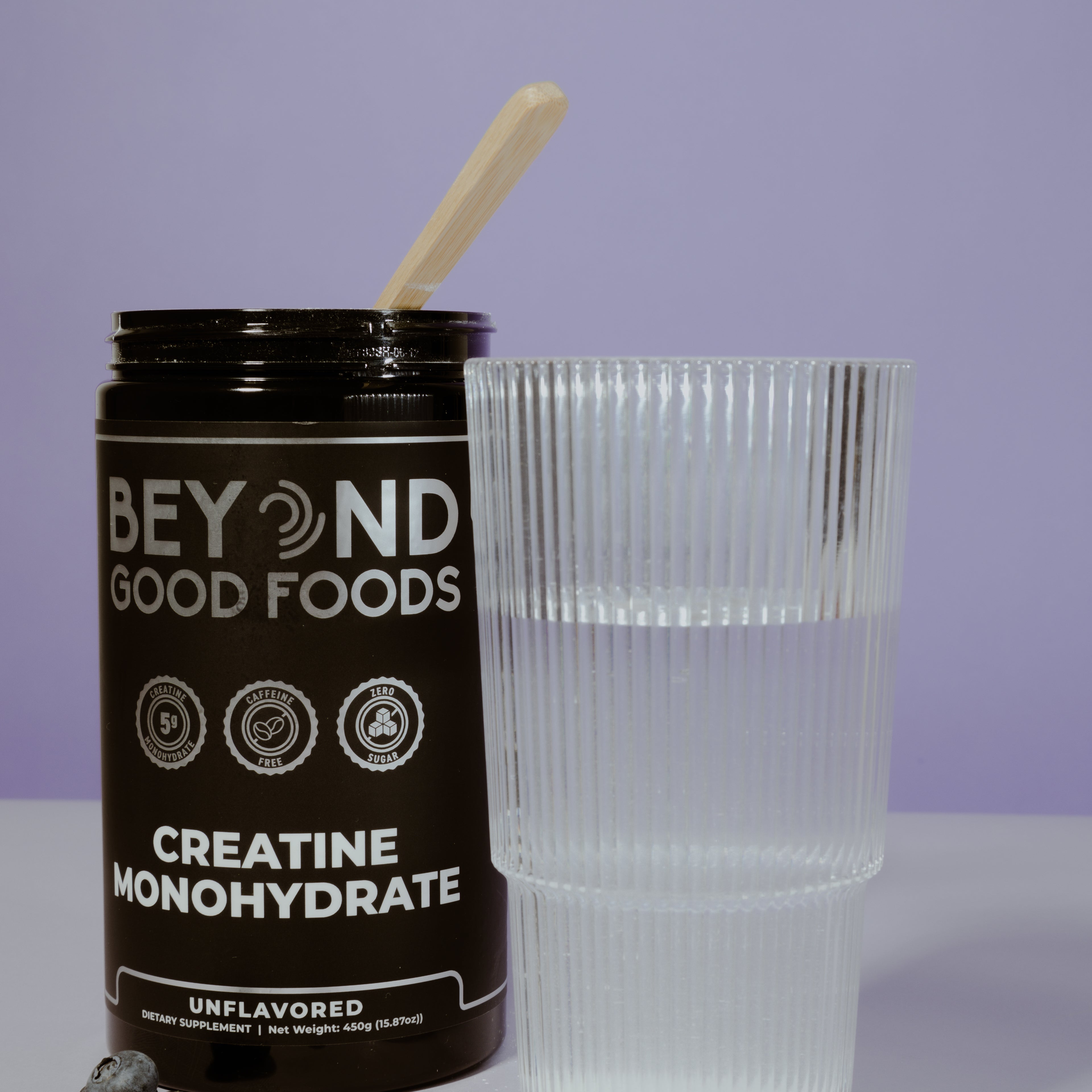 Bottle of Beyond Good Foods Creatine Monohydrate with a glass and blueberries on a light purple background