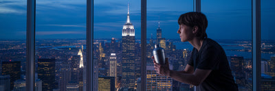 Person with protein shake overlooking city at night.