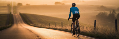 Cyclist watching sunrise over rolling hills.