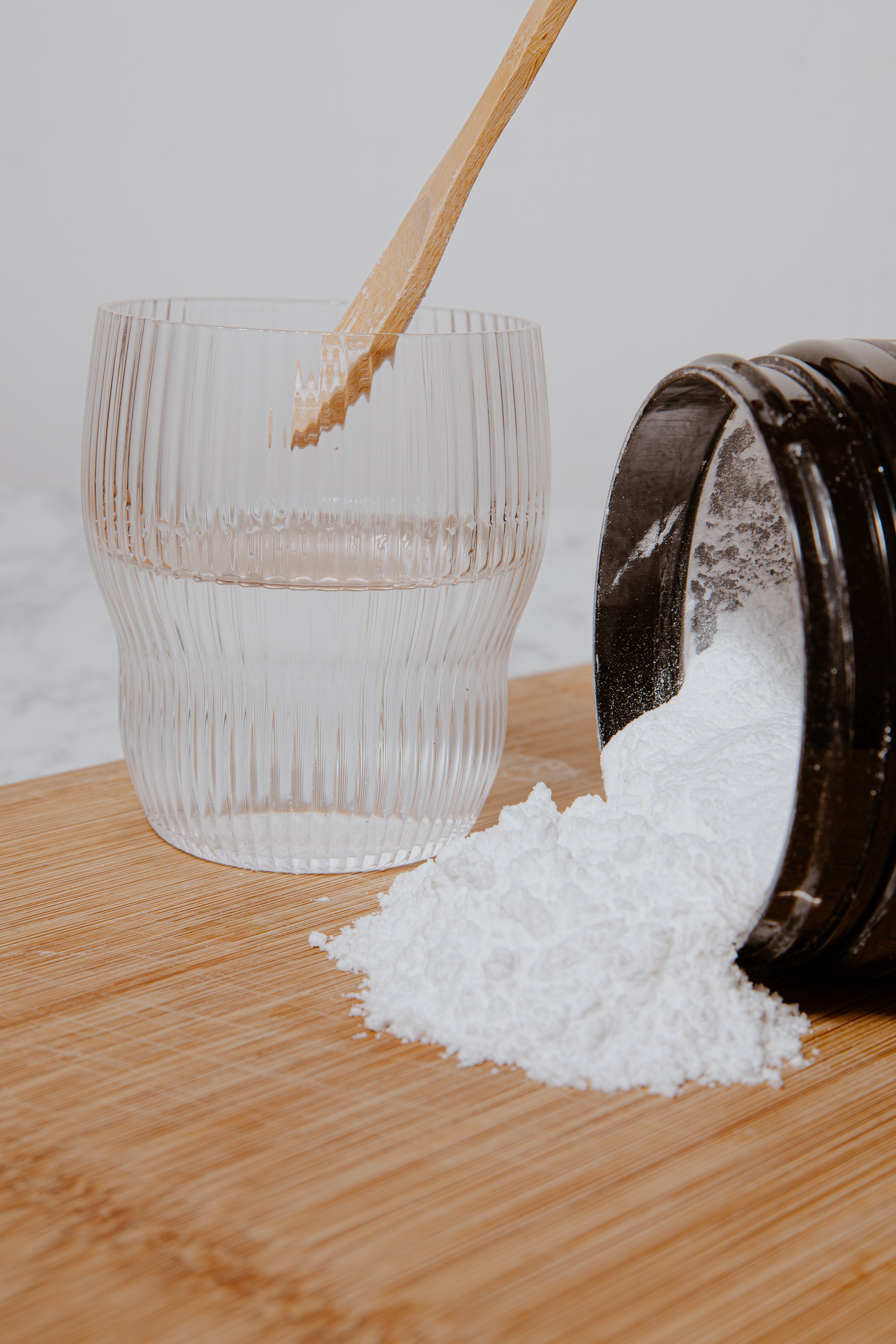 Wooden spoon scooping white powder from a container onto a glass on a wooden surface.